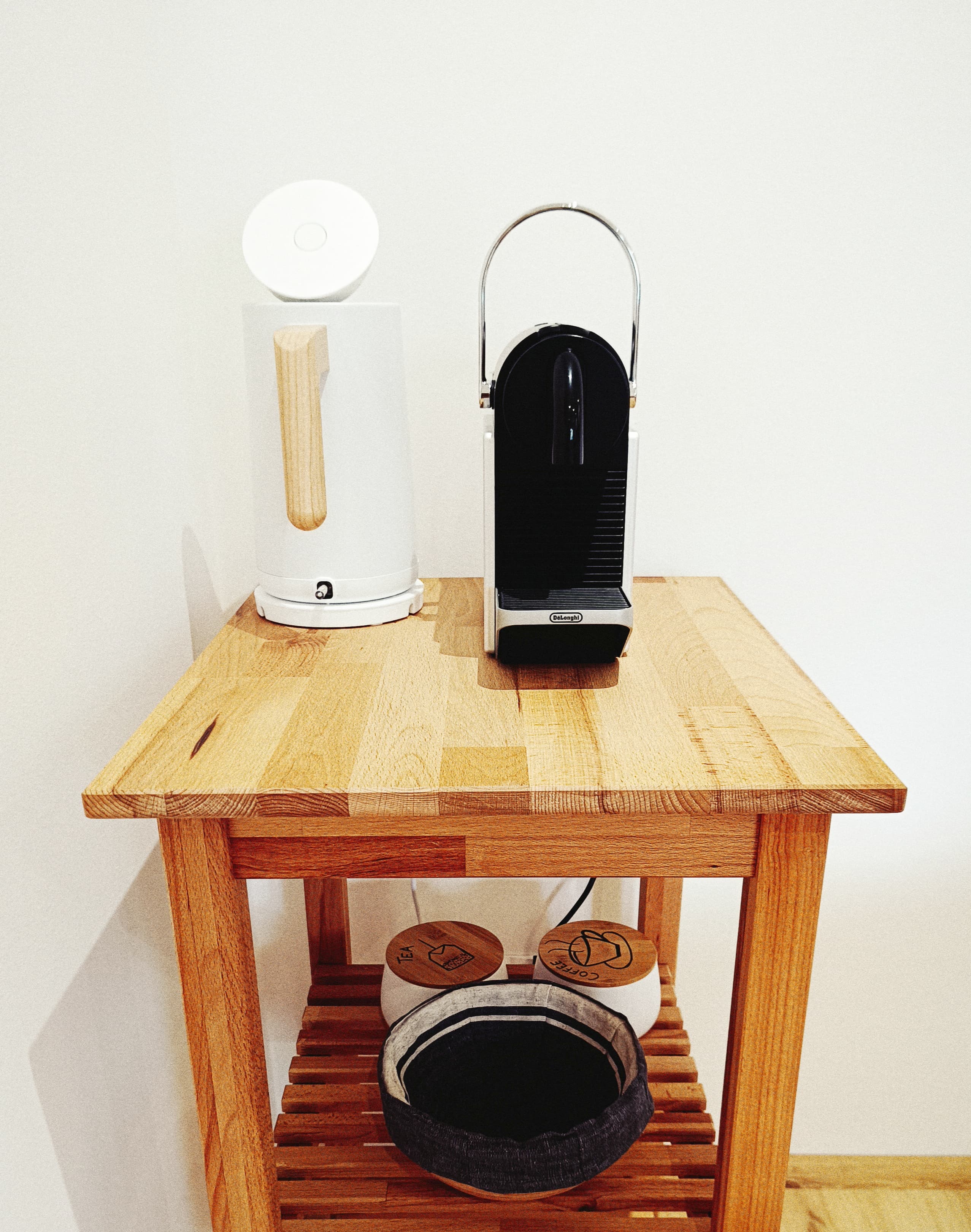 Holz-Beistelltisch mit einer eleganten Espressomaschine und einem stilvollen weißen Wasserkocher, ergänzt durch Tee- und Kaffeebehälter sowie einen Aufbewahrungskorb.