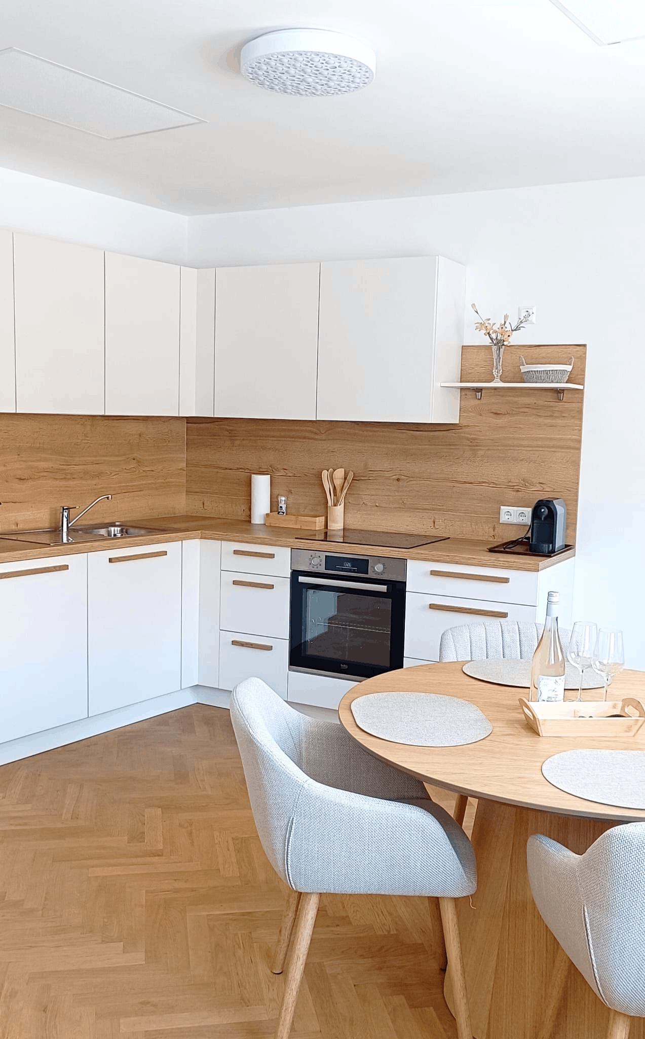 Helles Schlafzimmer mit frischer weißer Bettwäsche, gefalteten Handtüchern und einem stilvollen Holzschrank. Ein Fernseher hängt an der Wand über einem Topfpflanzen-Dekor.