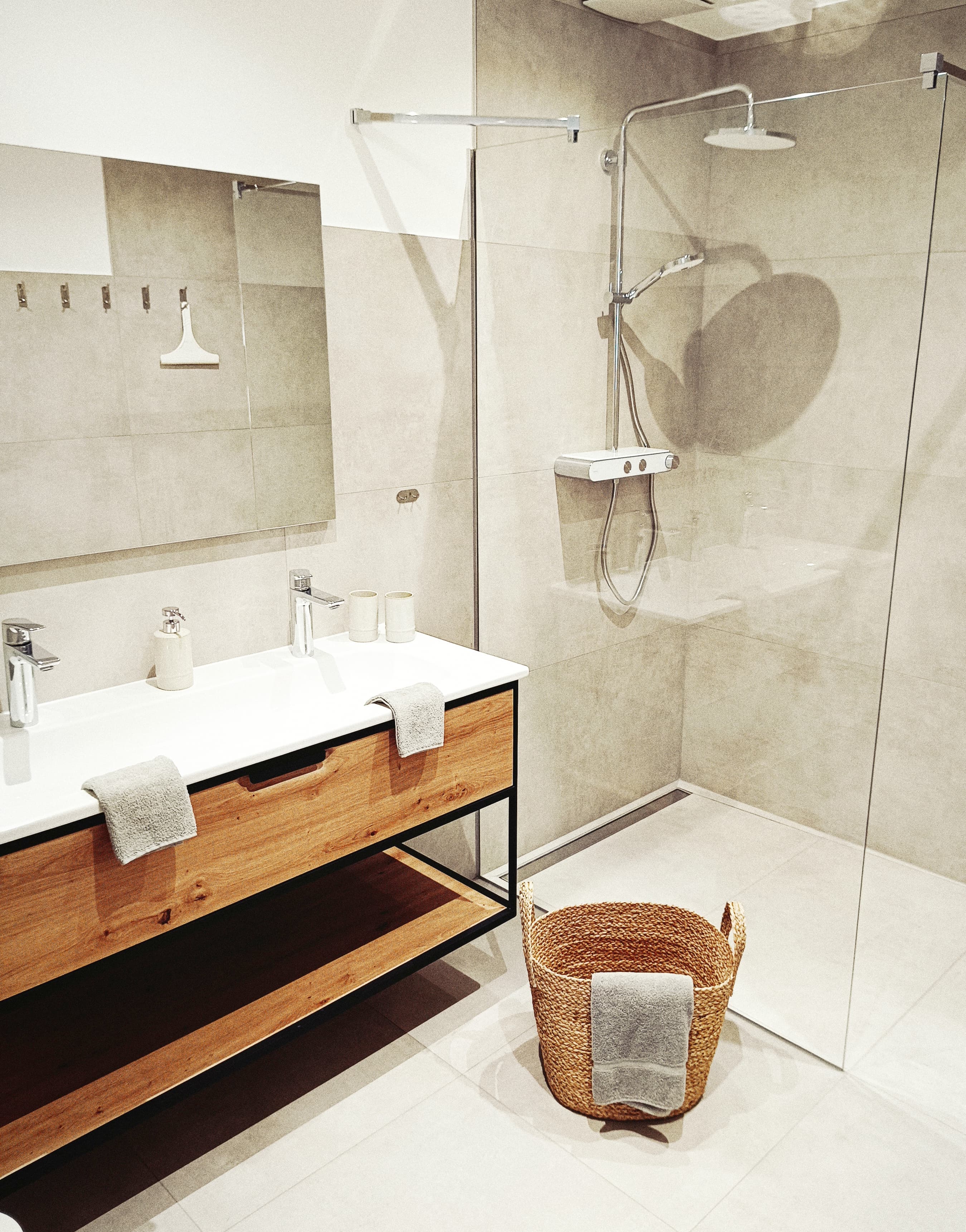 Modernes Badezimmerdesign mit einer begehbaren Dusche mit Glasgehäuse, einem Doppelwaschtisch mit Holzschränken und einem stilvollen, geflochtenen Wäschekorb. Clean lines and neutral color tones.