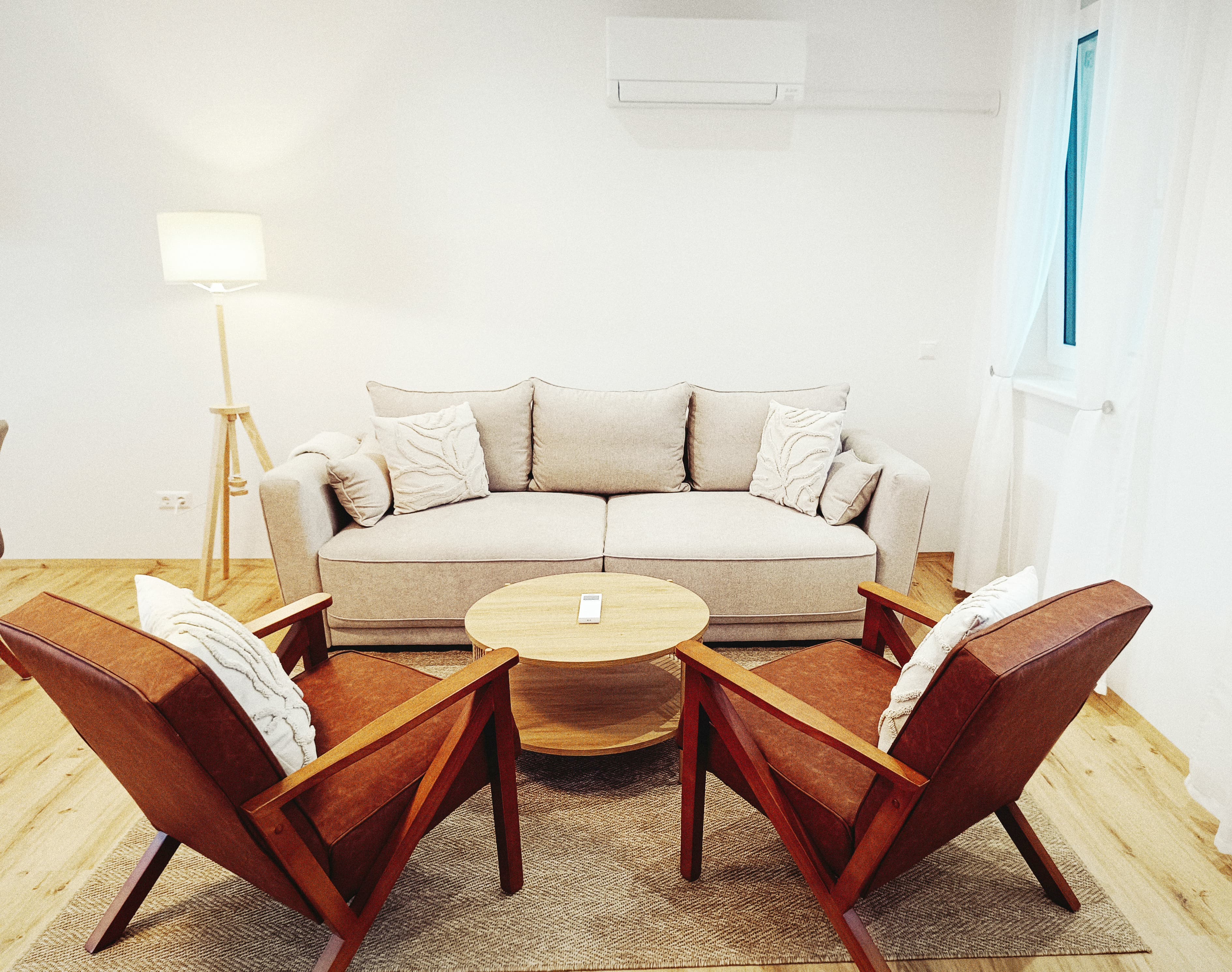 Gemütliches Wohnzimmer mit einem beigen Sofa, zwei braunen Sesseln, einem runden Holztisch und einer Stehlampe. Soft lighting creates a warm, inviting ambiance.