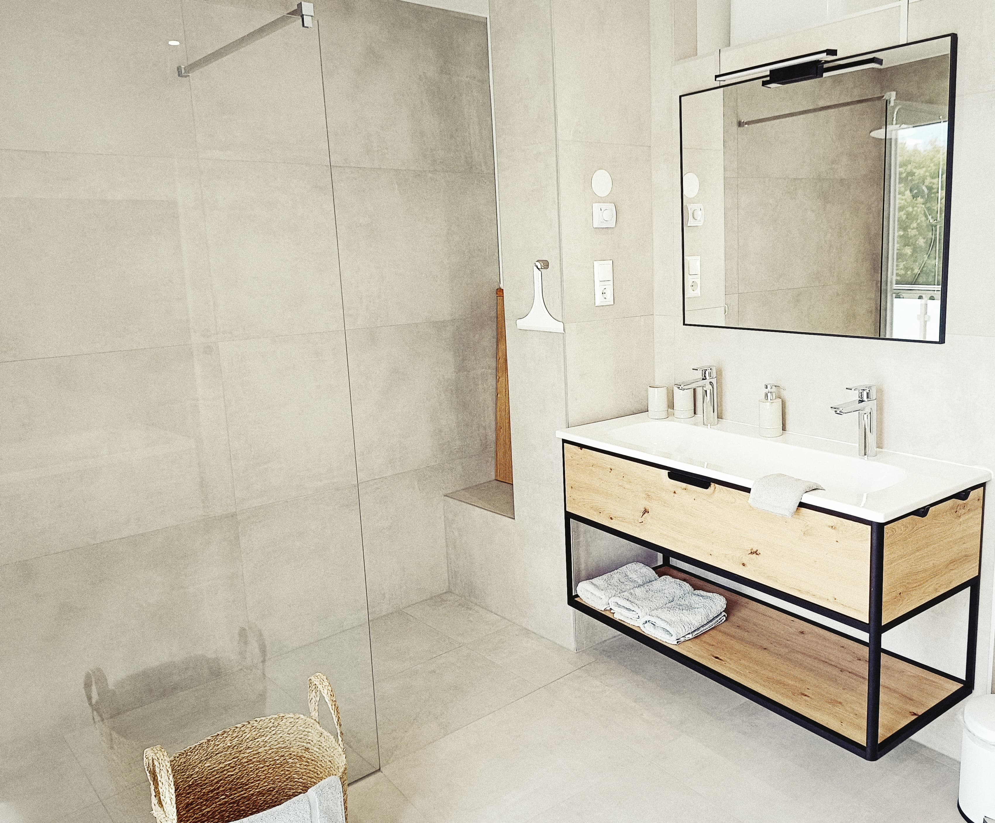 Modernes Badezimmer mit einer begehbaren Glasdusche, beigen Fliesen und einem Holzwaschtisch mit Doppelwaschbecken. Bright, minimalistic design with a calming atmosphere.