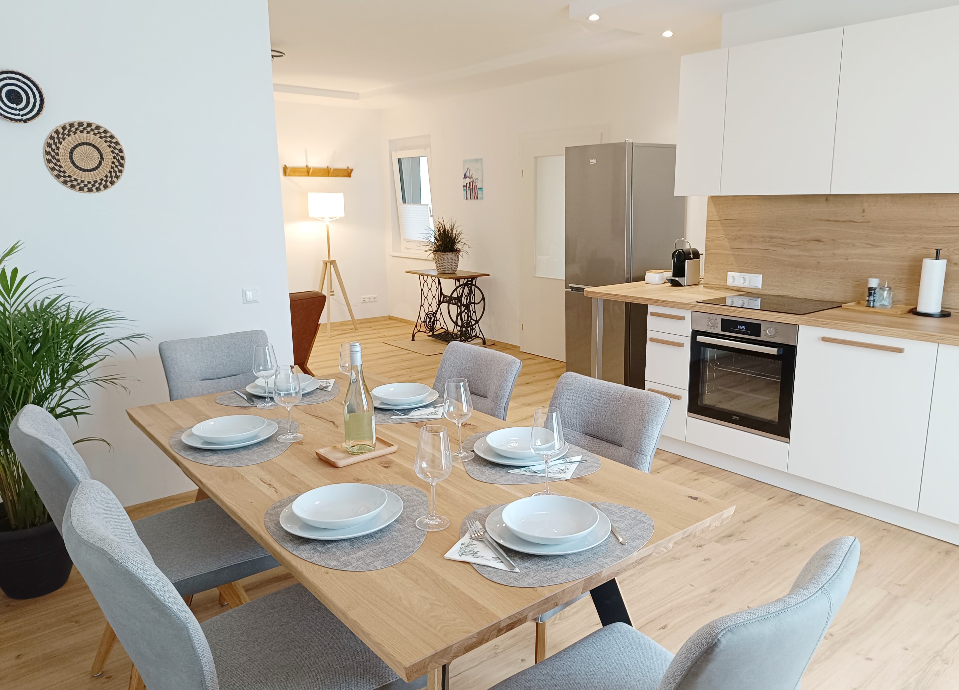 Zeitgenössischer Essbereich und Küche mit einem Holztisch, sechs grauen Stühlen, gedeckt mit Tellern und Gläsern. Light wood flooring, white cabinets, modern decor. Peaceful ambiance.